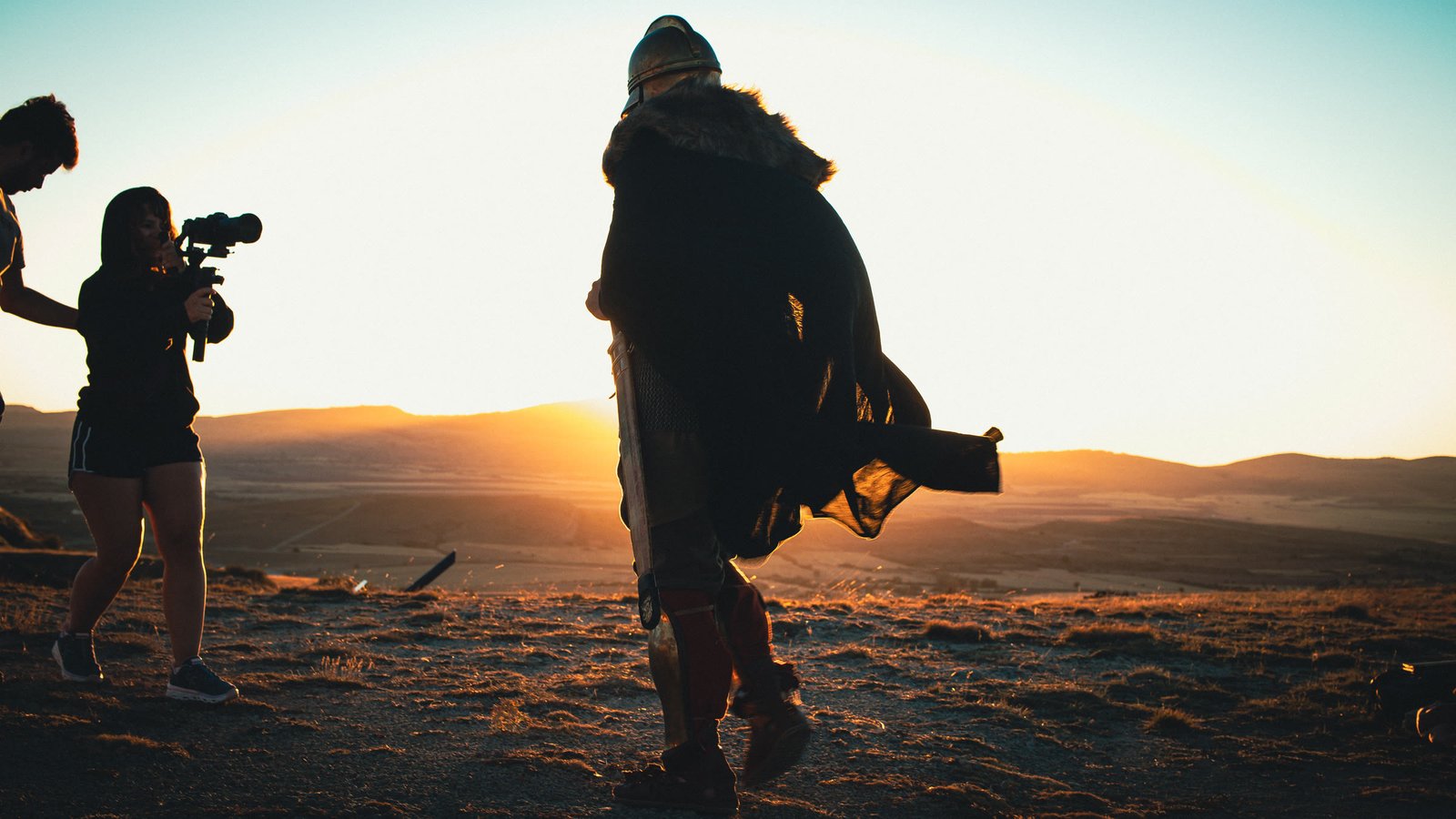 Rodaje al atardecer: una figura con capa y un operador de cámara filmando.